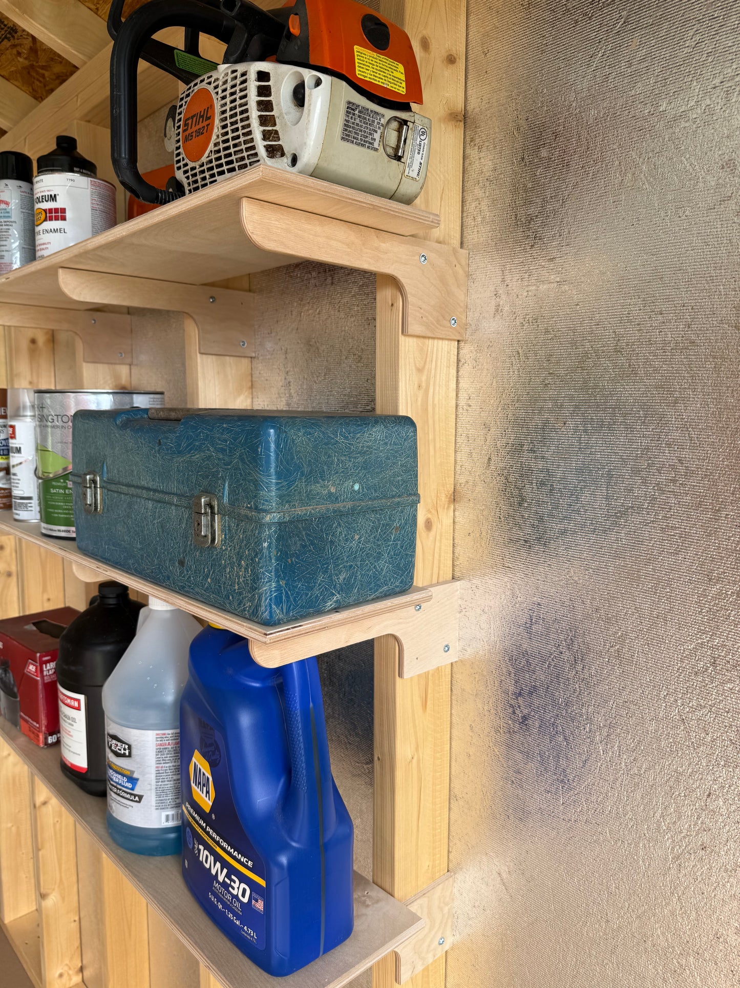 Wooden shelf with tools and supplies on a wall in a storage shed.