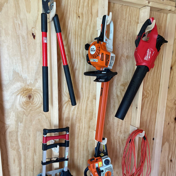 1. Various tools and equipment neatly organized on hooks in a shed, including power tools, leaf blowers, chainsaws, and extension cords. 2. Efficiently arranged shed with tools and equipment hanging on hooks, featuring power tools, leaf blowers, chainsaws, and extension cord storage. 3. Neatly displayed tools and equipment on hooks in a shed, including power tools, leaf blowers, chainsaws, and organized extension cord storage.