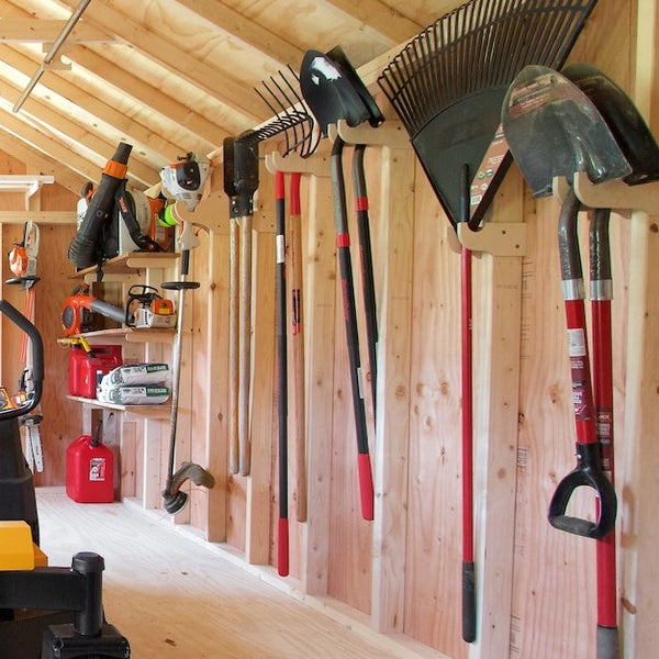 Garden tool rack with shovels and other tools mounted on a wall in a yard shed.