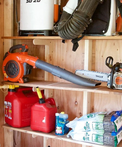 Shed storage shelves holding a leaf blower, chainsaw, fuel cans, and other outdoor equipment, keeping tools organized and easily accessible.