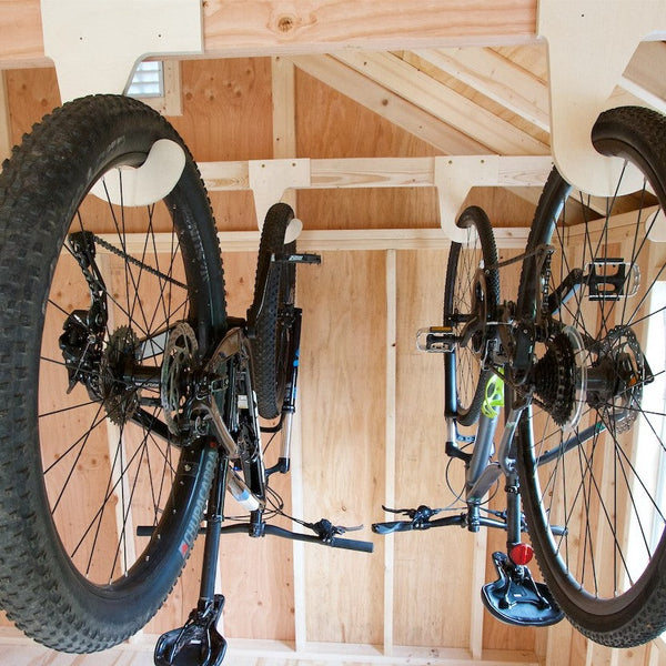 Two bikes hanging using the My S.O.S. bike organizers . A bike hanging from the ceiling in a shed. Efficient bike storage solution using a wood rack in a yard shed.