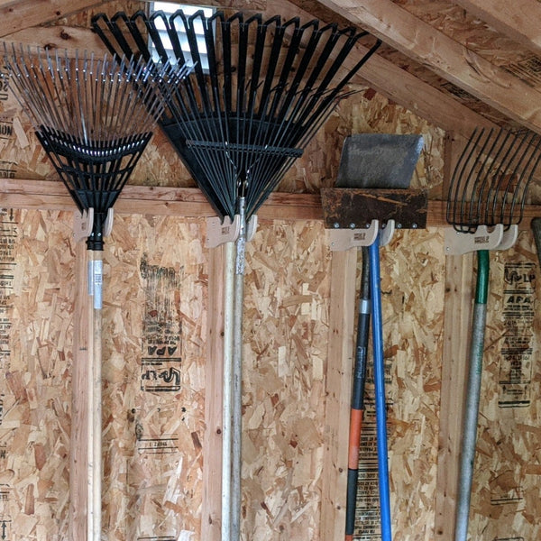 Garden tool rack with shovels and other tools mounted on a wall in a yard shed.